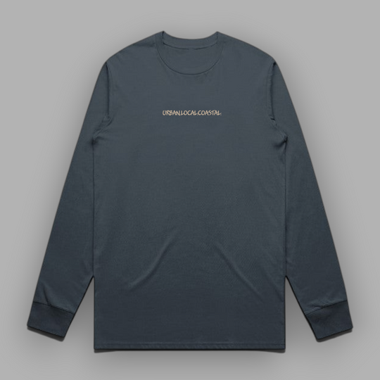 Front view of a petrol blue long-sleeve cotton tee with sand-colored URBAN.LOCAL.COASTAL. embroidery centered on the chest.