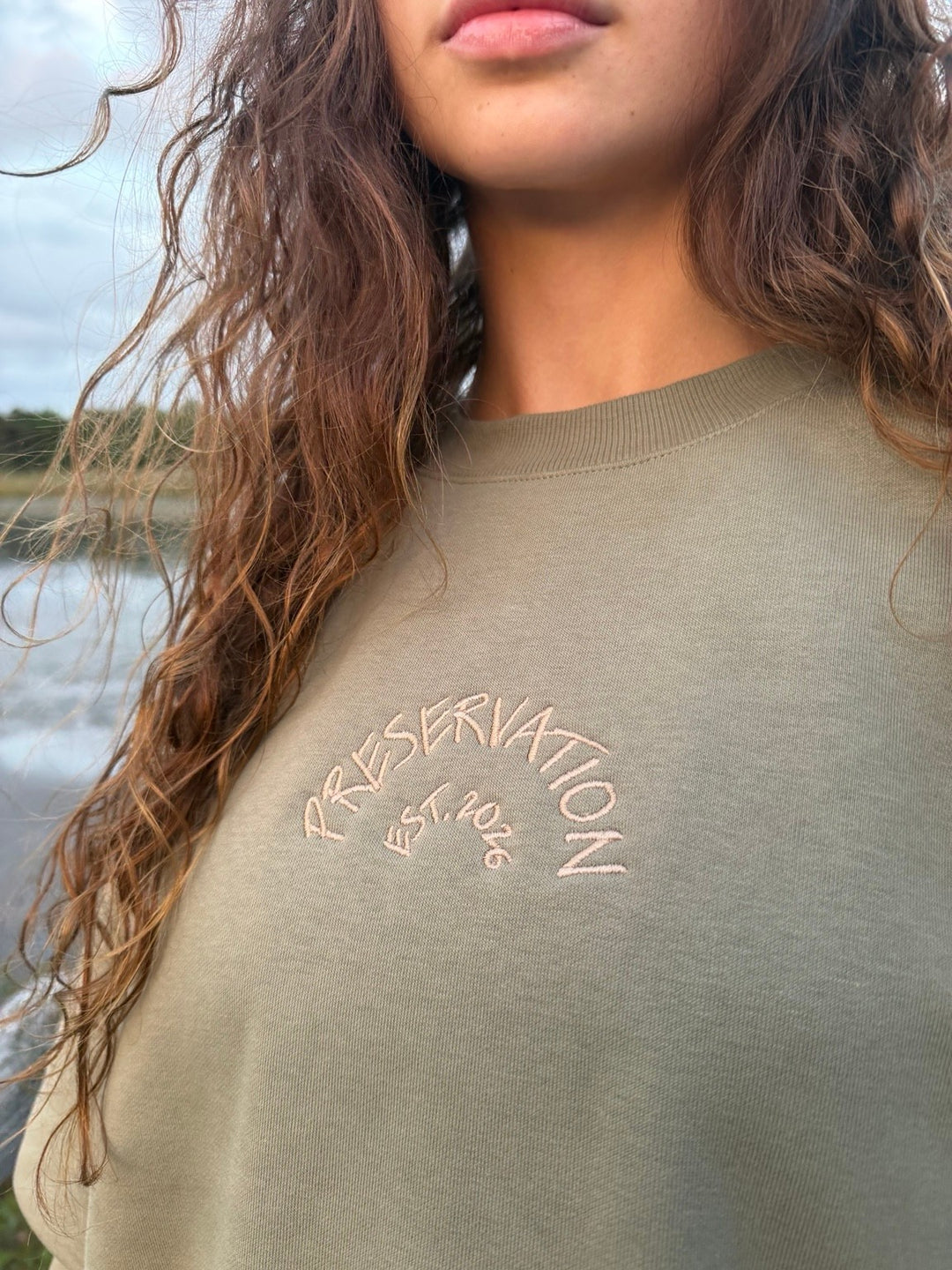area 609 eucalyptus heavyweight fleece crewneck sweatshirt with sand arch embroidery on chest worn by a woman