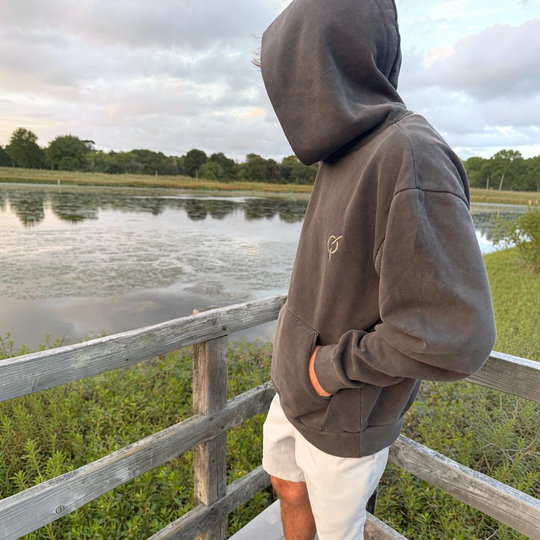 area 609 heavyweight pigment black hoodie with core emblem on chest, worn by a person on a wooden pier by a lake
