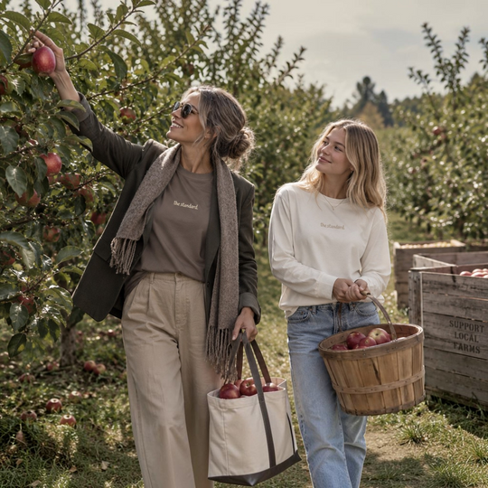 Two women wearing area 609 The Standard long sleeve tees in an apple orchard, one in taupe and one in cream.