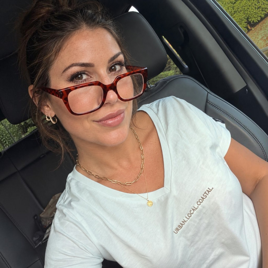 Woman wearing an area 609 white cotton V-neck shirt with URBAN. LOCAL. COASTAL. embroidery in sand-colored thread.